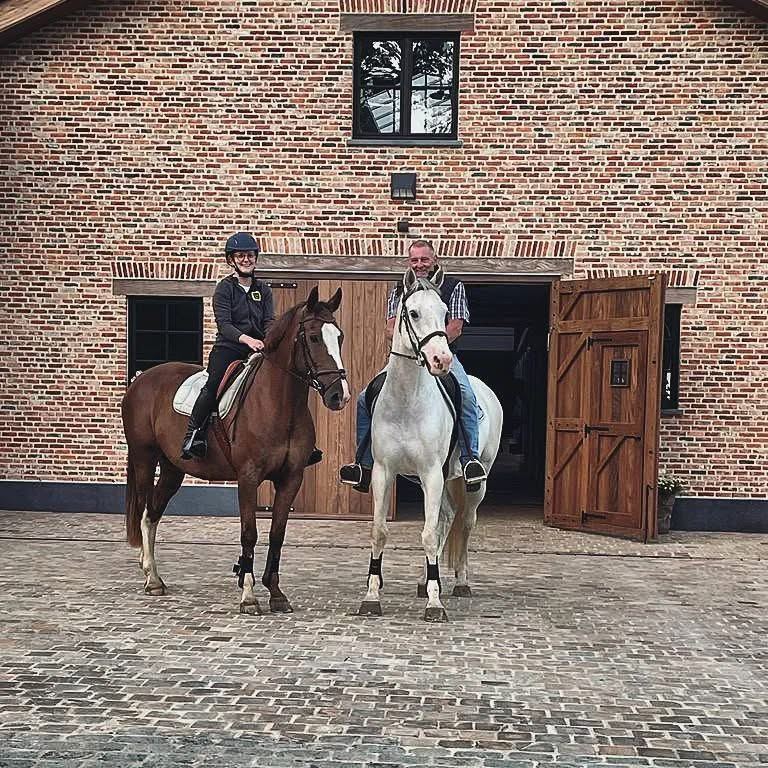 Marieke en haar vader te paard voor een bakstenen stal